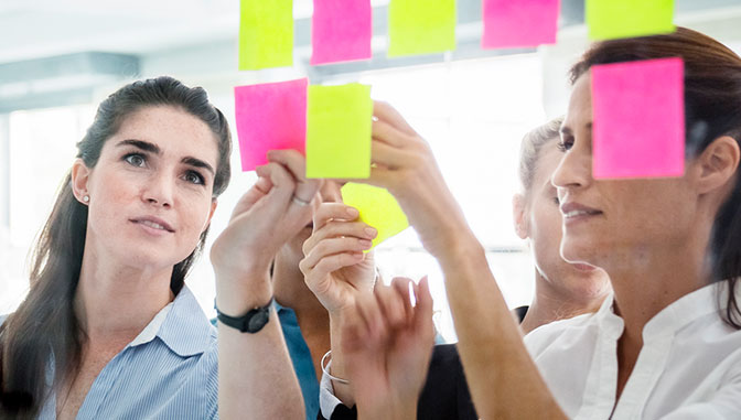 mujeres jóvenes profesionales creando un gráfico kanban con post its