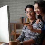 female leaning over male shoulder to give credit card numbers, both in front of computer