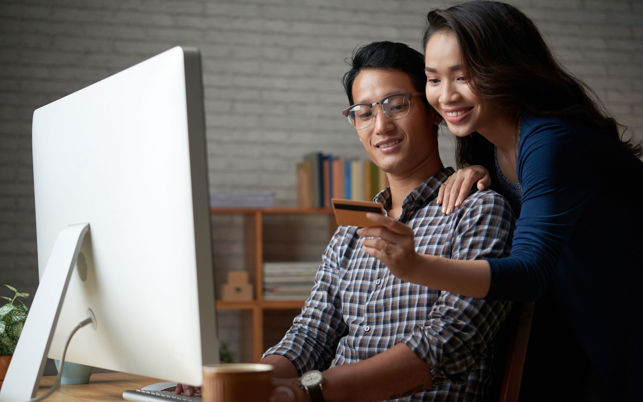 female leaning over male shoulder to give credit card numbers, both in front of computer