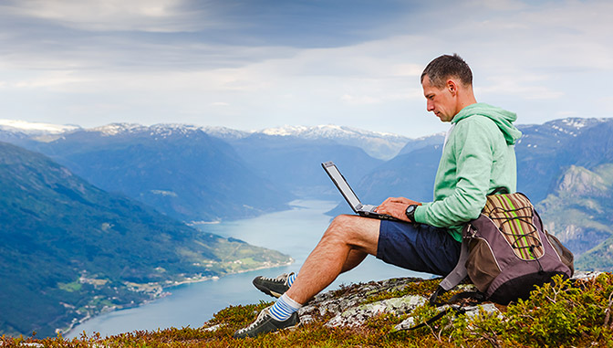 Estudiante en la cima de una montaña con un portátil