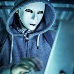 man wearing mask in a hoodie on laptop