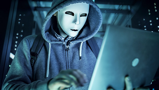 man wearing mask in a hoodie on laptop