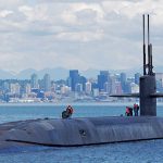 submarine emerging from the water in front of a city