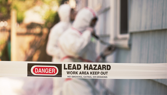 danger tape for lead hazard and workers in white hazmat suits