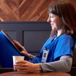 female nurse in scrubs practicing self care, drinking coffee