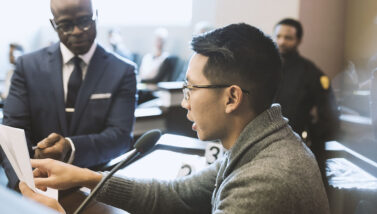 A man reading a document on the stand at a trial