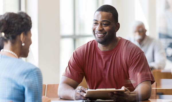 Man with clipboard speaking with woman across from table