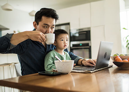 veterano de guerra utilizando un ordenador portátil con su hijo en el regazo mientras toma café