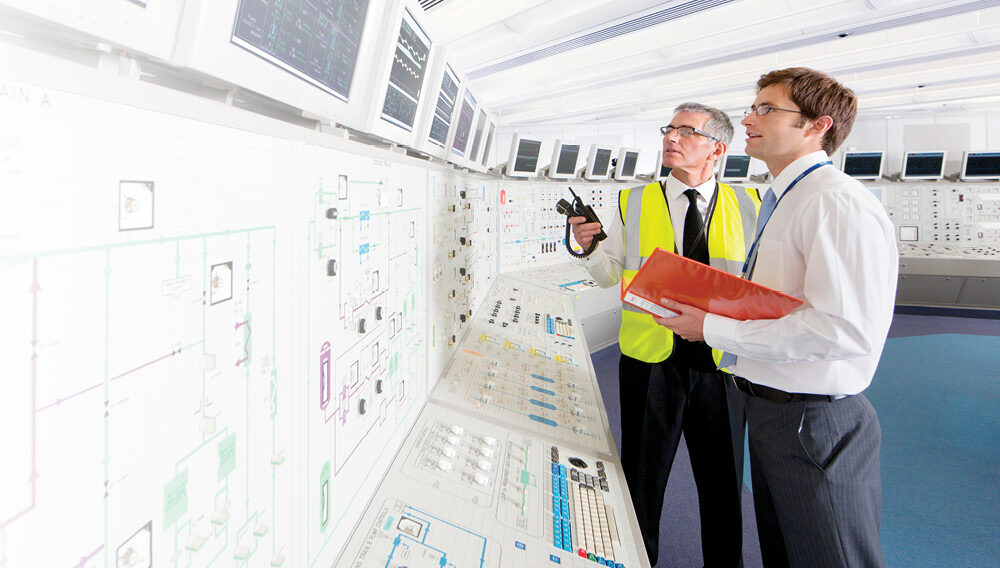Two engineers monitor reactor readings from displays in a nuclear power plant control room.