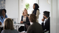 woman in leadership role standing in front of board room speaking