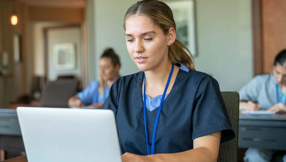 woman in scrubs studying on laptop