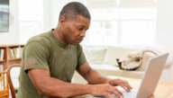 male in army green shirt studying on laptop