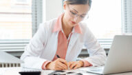 mujer con bata blanca de laboratorio tomando notas en un escritorio