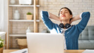 Young woman leaning back from her desk, hands laced behind her head and eyes closed.