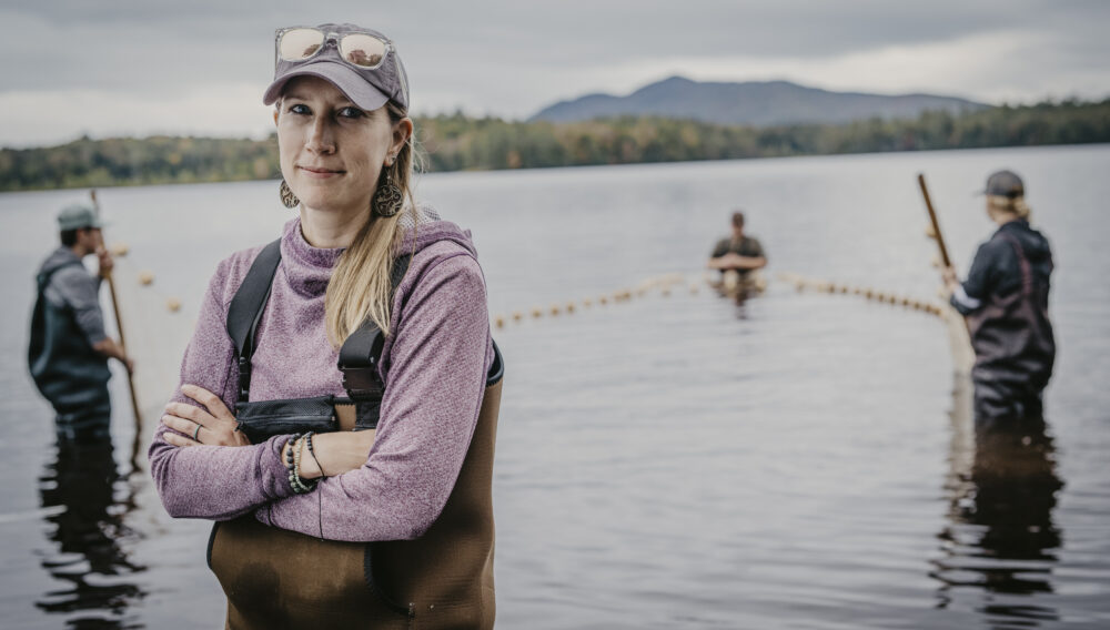men and women standing in lake with waders on, woman in foreground looking at camera with arms folded