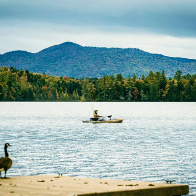 person in a canoe in a lake surrounded by trees and mountains