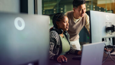 A pair of smiling co-workers huddled around a computer screen