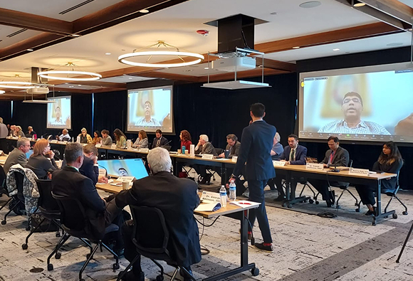 conference room with attendees sitting in a panel observing someone giving a presentation