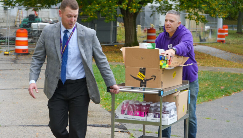 Ryan Meikle, Troy High School assistant principal (left), and Zach Patterson, Excelsior University community engagement group co-chair (right), deliver Snacks for Students donations to Troy High School.