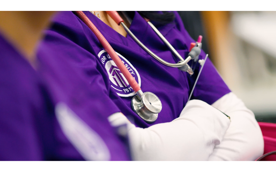 A nurse with stethoscope and Excelsior University scrubs in a clinical practice setting.