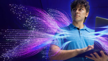 Graphic representation of an IT professional on a laptop, surrounded by purple and blue luminescent fibers representing artificial intelligence