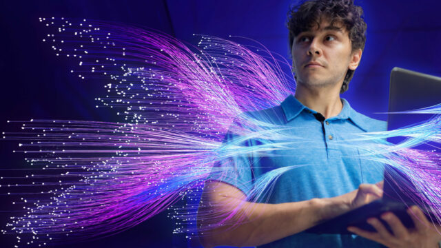 Graphic representation of an IT professional on a laptop, surrounded by purple and blue luminescent fibers representing artificial intelligence