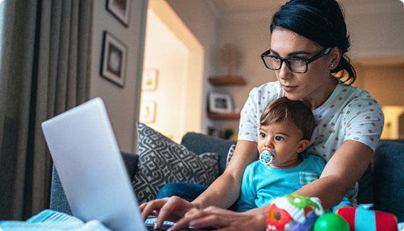 A mother with her baby on her lap typing on a laptop