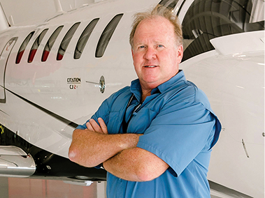 Lawrence Warner standing with arms crossed in front of an aircraft.