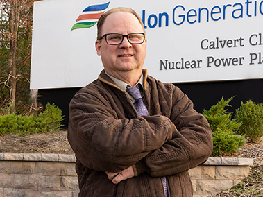 William Klee standing with arms crossed in front of the Calvert Cliffs Nuclear Power Plant sign.