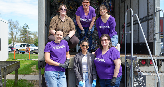 Excelsior University staff and volunteers in matching purple shirts pose while loading donations into a truck.