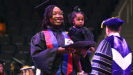 An Excelsior University graduate carries a baby at a Commencement ceremony.