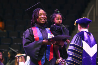 An Excelsior University graduate carries a baby at a Commencement ceremony.